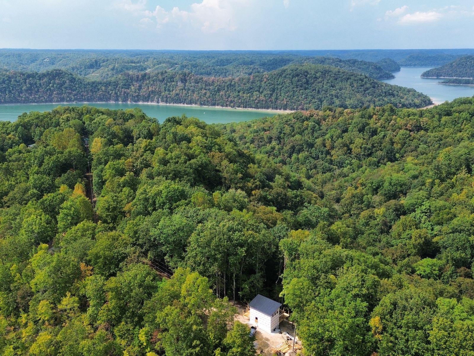 Drone view of the first house, roof on, in the trees on the ridge, with Center Hill Lake beyond the far hills